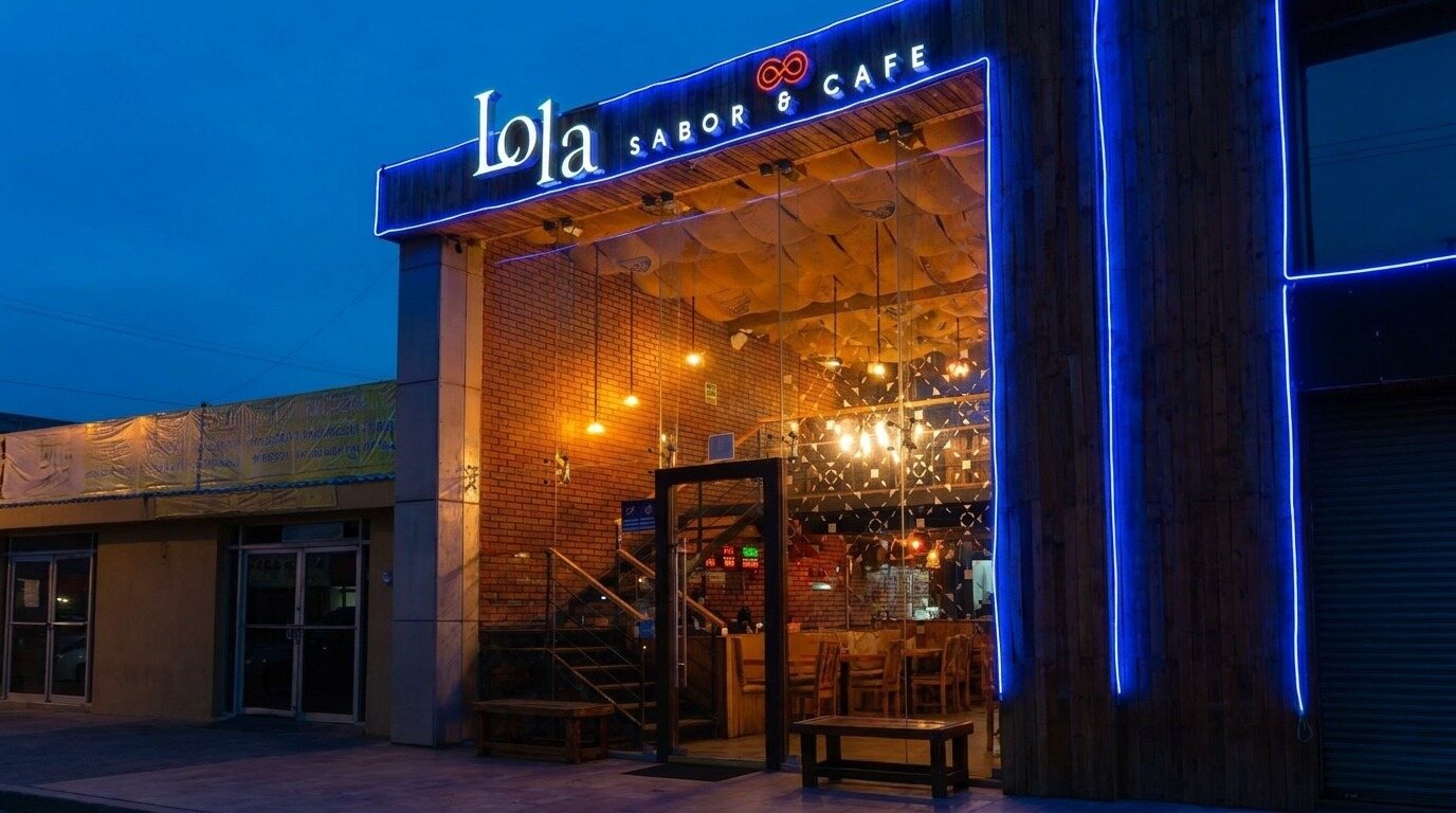 Fachada nocturna de Lola Sabor y Café en el centro de Rosarito: letrero «Lola Sabor & Café» con neón azul, frente de vidrio, muro de ladrillo y escalera al segundo piso