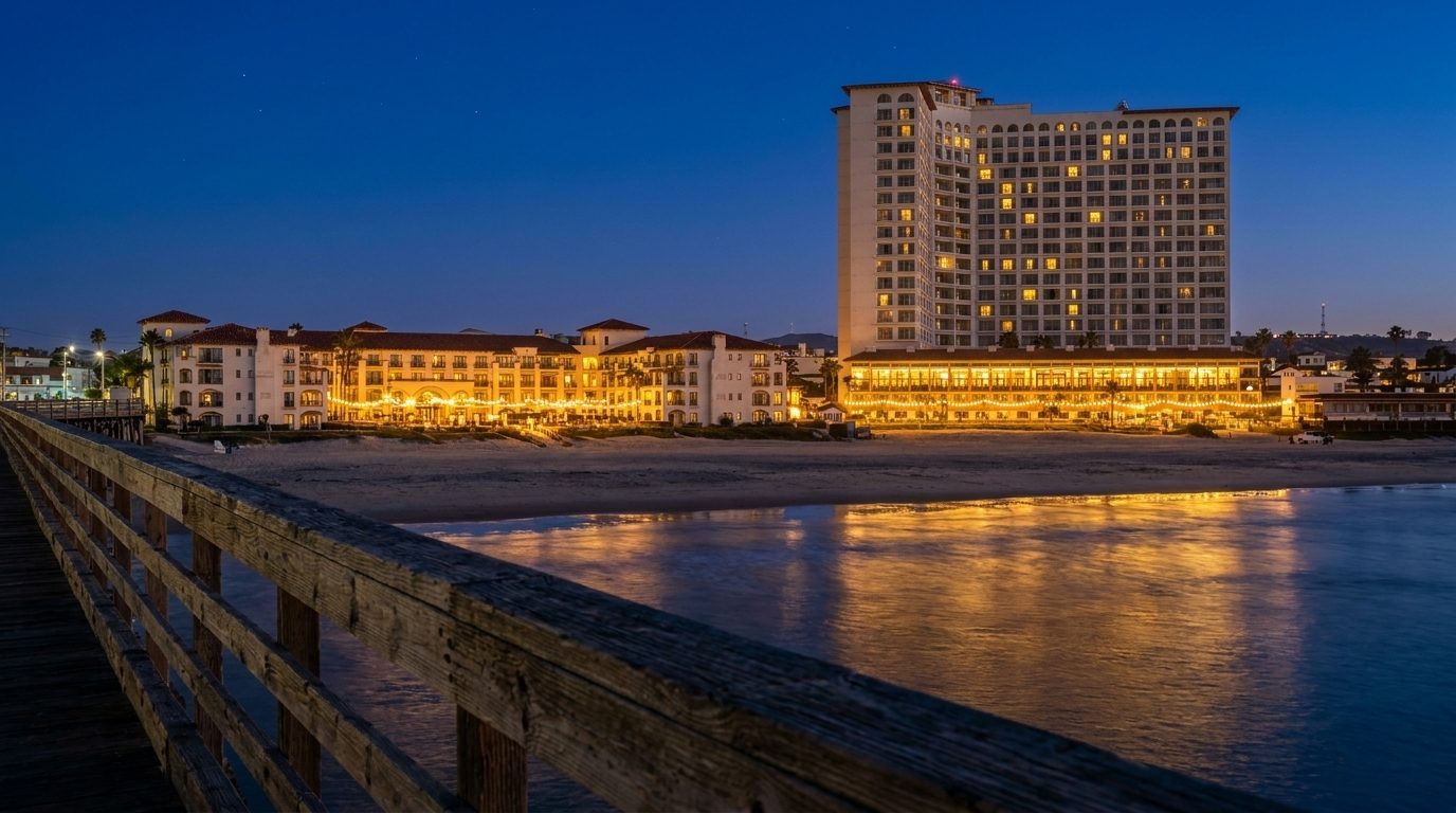 El Rosarito Beach Hotel de noche visto desde el muelle, con las ventanas y las terrazas iluminadas reflejadas en la arena mojada